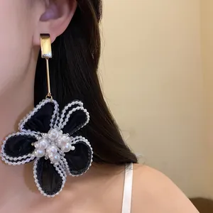 Detailed view of an elegant black snow yarn flower drop earring with pearl bead outlines.