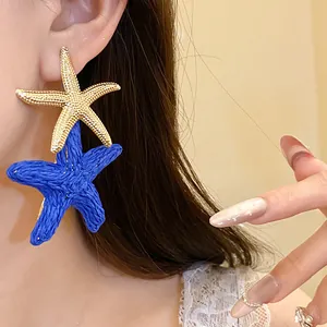 Dettaglio di orecchini a stella marina in rafia blu e oro indossati