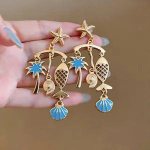Close-up of gold enamel sea life dangle earrings with starfish and palm charms