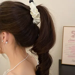 Detail view of a cream satin scrunchie banana clip holding a high ponytail securely.