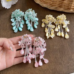 Vibrant handmade flower tassel earrings in pink, green, and yellow displayed on wood.