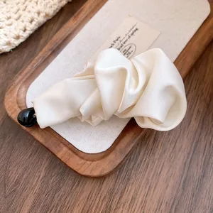 Macro view of an elegant cream satin banana hair clip placed on a rustic wooden tray.