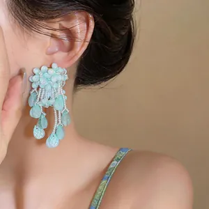 Close-up detail of oversized pale blue flower tassel earrings with white beads and petals