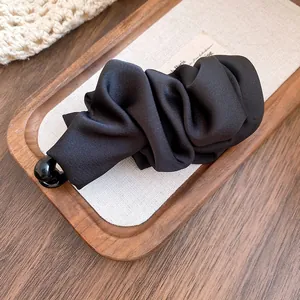 Detailed close-up of a black ruffled satin banana hair clip on a wooden tray