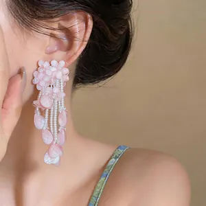 Close-up detail of stylish pink flower tassel earrings with white pearl accents on model