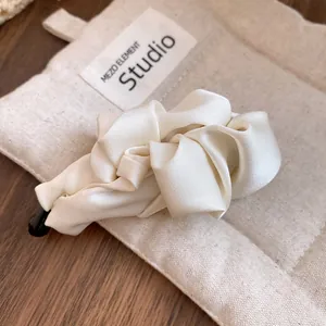 Close-up of an elegant cream satin fabric twist hair clip on a beige canvas pouch