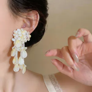 A detailed view of elegant cream yellow floral tassel drop earrings worn by a model