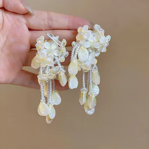 Detailed macro view of cream pearlescent floral tassel earrings with beaded drops.