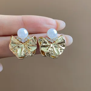 Dettaglio di eleganti orecchini in oro plissettati con inserto di perla e zircone