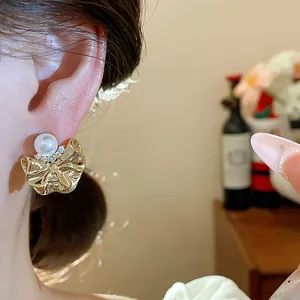 Dettaglio ravvicinato di orecchini a fiore dorato stropicciato con perla e zircone