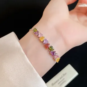 Gros plan de pierres de zircon colorées en forme de cœur sur un bracelet en argent au poignet.
