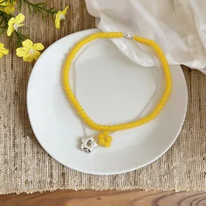 Close-up of a double-layered necklace featuring yellow glass beads and flower pendants