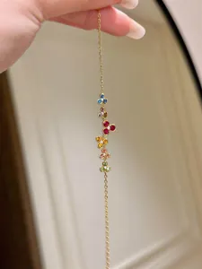 Close-up of vibrant multi-colored gemstone flower charms on a gold chain bracelet.