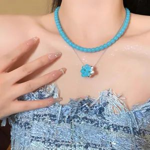 Detail of a blue glass bead and silver chain necklace with a flower pendant on a model.