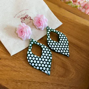 Close-up of retro green and white polka dot teardrop earrings with pink rose studs