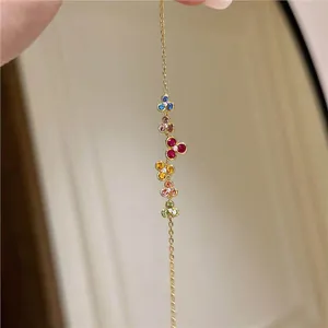 Close-up of a delicate gold bracelet featuring colorful gemstone flower charms.