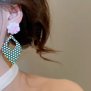 Detail view of retro pink flower earrings with a green and white polka dot drop design