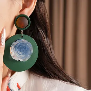 Close-up of retro ethnic style green resin earrings with a blue rose centerpiece
