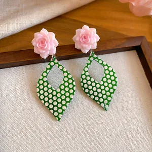 Detailed macro view of vintage pink flower earrings with green white polka dot dangle.