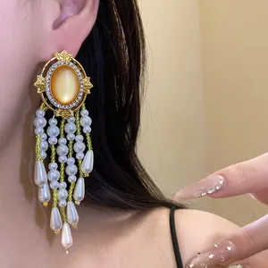 Detailansicht goldener Vintage-Ohrringe mit gelbem Katzenaugenstein und Perlenquasten.