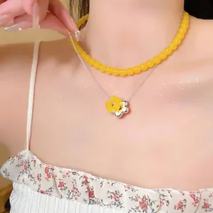 Close-up of French style layered necklace with yellow glass beads and flower pendant.