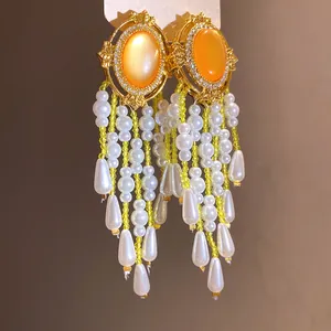 Makro-Detail von eleganten goldfarbenen Quastenohrringen mit orangefarbenen Steinen