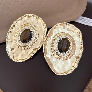 Close-up of vintage hammered gold oval stud earrings with center resin stone and rhinestones.