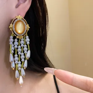 Detailaufnahme eleganter goldfarbener Quastenohrringe mit weißen Perlen und orangem Stein