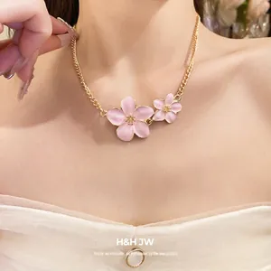 Elegant gold necklace featuring two pink enamel cherry blossom pendants on a woman
