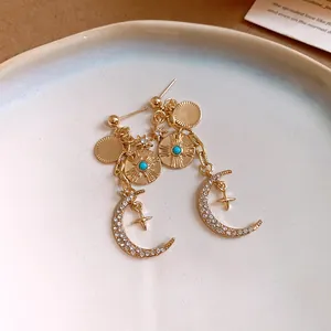 Gros plan de boucles d'oreilles dorées de style français avec motifs lune et soleil en strass