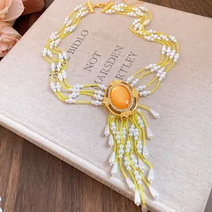 Detailansicht eines luxuriösen Perlen-Chokers mit orangefarbenem Stein und Quasten