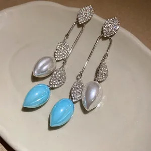 Detail view of vintage style rhinestone leaf drop earrings with blue and white pearls.