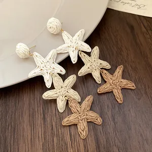 Vue détaillée de boucles d'oreilles pendantes étoile de mer en raphia tissé à la main.