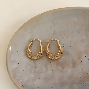 Detailed macro view of gold-plated twisted geometric hoop earrings with zircon stones
