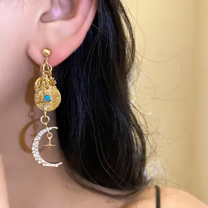 Détail d'une boucle d'oreille dorée de style français avec croissant de lune et strass brillants.
