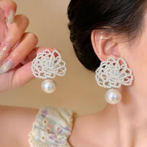 Macro detail of elegant hand-beaded flower earrings with a large white pearl drop on model