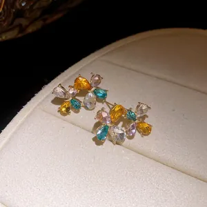 Detailed macro view of colorful zirconia flower stud earrings on beige cushion.