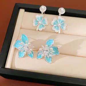 Detailed view of blue enamel flower and clover stud earrings with pearls and zircons