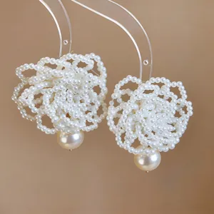 Close-up of intricate white beaded flower earrings with a hanging teardrop pearl.