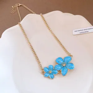 Detailed view of gold clavicle chain necklace featuring two blue enamel flower pendants