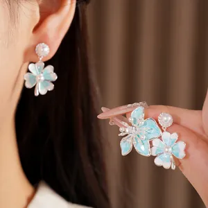 Detailed view of blue enamel flower earrings with pearls and zircons on model's ear