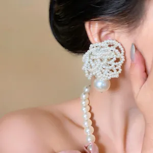 Detailed close-up view of elegant large white beaded flower pearl earrings worn by a model