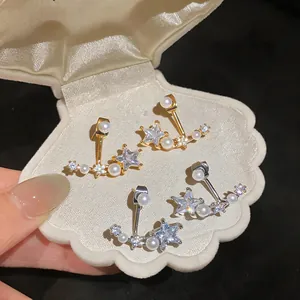 Close-up of star-shaped zircon and pearl stud earrings presented in a shell box.