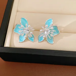 Close-up view of blue enamel flower stud earrings with heart-shaped zircon and pearls