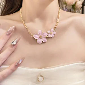 Detail view of an elegant pink enamel flower necklace on a golden chain worn by a model