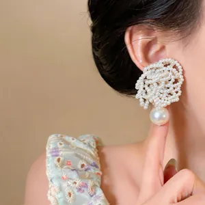 Close-up of elegant beaded flower pearl stud earrings with large drop pearls on a model