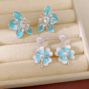 Close-up of elegant blue enamel flower and lucky clover earrings with pearls and zircons