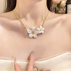 Close-up of elegant gold chain necklace with white enamel flower pendants worn by model