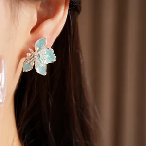 Close-up view of elegant blue enamel flower stud earrings with pearls and zircon on an ear