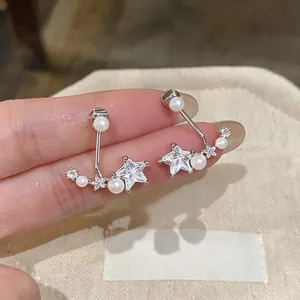 Macro view of star-shaped zircon earrings with delicate pearl accents on silver pins.